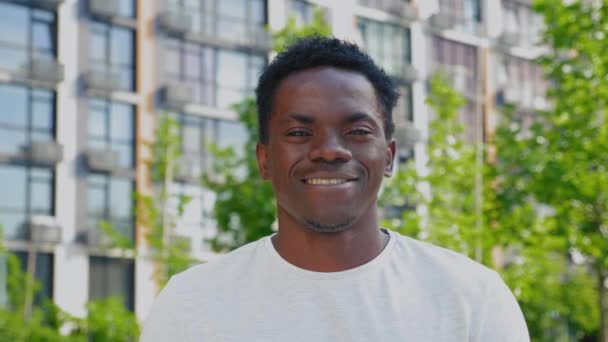 Close-up glimlachen afro-amerikaanse man kijkt camera op achtergrond modern gebouw — Stockvideo