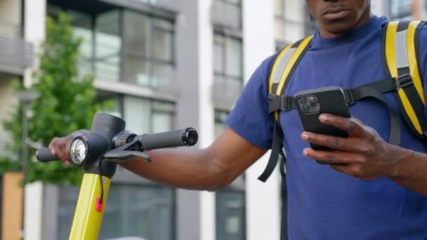 Hombre afroamericano mensajero entrega de alimentos con scooter eléctrico utiliza teléfono inteligente — Vídeos de Stock