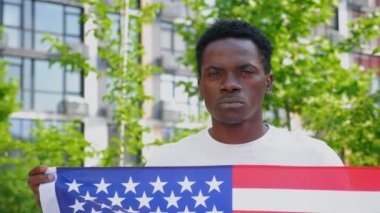 Amerikan bayrağını tutan Afro-Amerikan adam kameraya bakıyor.