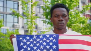 Amerikan bayrağını tutan Afro-Amerikan adam kameraya bakıyor.
