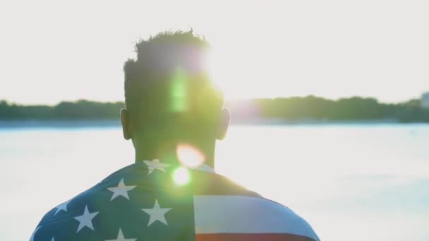 Vista posterior afroamericano hombre étnico negro con bandera de EE.UU. en el hombro se ve amanecer — Vídeos de Stock