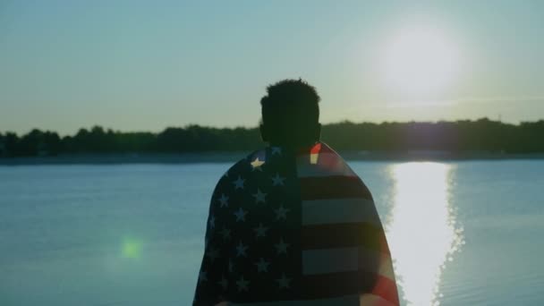 Un homme afro-américain avec le drapeau américain sur les épaules regarde loin au lever du soleil — Video