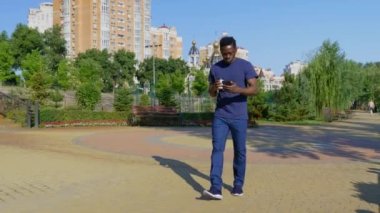 Afro-Amerikalı adam elinde kahve ya da çay olan beyaz bardakla cep telefonu kullanıyor.