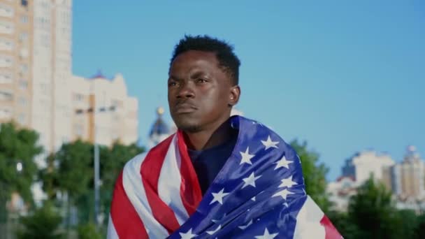 Patriota afro-americano caminando calle con bandera americana en la espalda en verano — Vídeo de stock