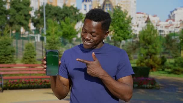 Uśmiechnięty afro-amerykański człowiek palec wskazuje smartfon wyświetlacz z zielonym ekranem — Wideo stockowe