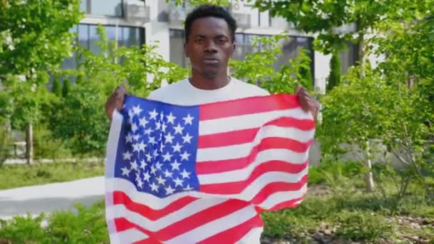 Powiększ afro-amerykańskiego mężczyznę trzymającego amerykańską flagę, wygląda jak kamera i mówi USA — Wideo stockowe