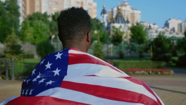 Volver ver patriota afro-americano hombre caminando calle con bandera americana en la espalda — Vídeo de stock
