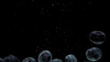 Yavaş hareket eden mavi erikler siyah arkaplanda saydam suya düşüyorlar.