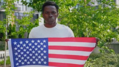Amerikan bayrağı taşıyan Afro-Amerikan bir adam ve yazın kameraya bakıyor.