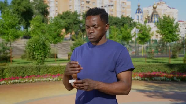 Retrato hombre adulto afroamericano de pie en el parque con auriculares inalámbricos — Vídeos de Stock