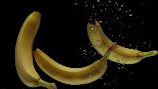 慢动作三只香蕉在黑色背景上掉进透明的水里 新鲜水果洒在水族馆里 健康食品 — 图库视频影像