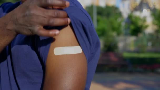 Афро-американец пациент показывает медицинскую штукатурку демонстрирует вакцину инъекции — стоковое видео