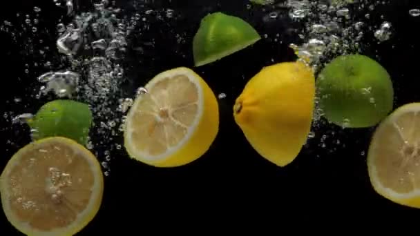 Citron och lime halvor faller i transparent vatten på svart bakgrund — Stockvideo