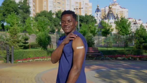 Pacjent z afro-amerykańskim człowiekiem pokazuje, że plaster medyczny wykazuje wstrzyknięcie szczepionki. — Wideo stockowe