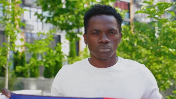 Close-up glimlachen afro-amerikaanse man met Amerikaanse vlag ziet er camera in de zomer — Stockvideo