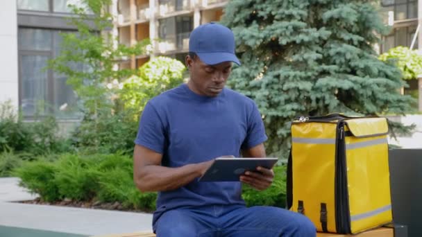 Aparat fotograficzny zoom afro-amerykański człowiek kurier dostawy wykorzystuje tablet patrząc aparat — Wideo stockowe