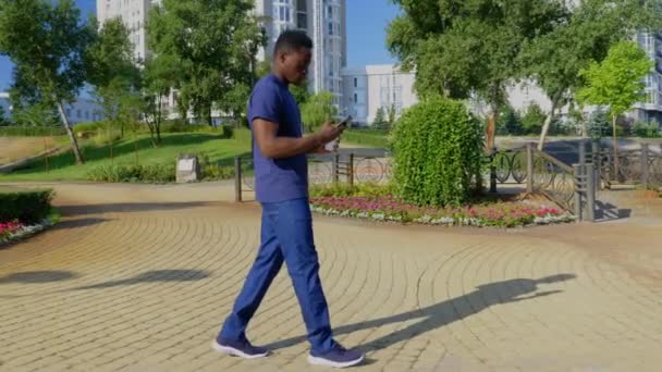 Afro-Amerikaanse man gebruikt mobiele telefoon met witte beker met koffie of thee in de hand — Stockvideo