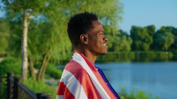 Sonriente hombre afroamericano con bandera americana en los hombros mira al amanecer — Vídeo de stock