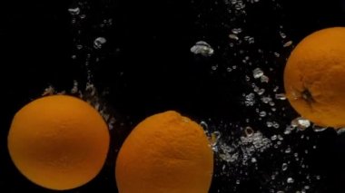 Yavaş çekim üç portakal siyah zemin üzerinde şeffaf suya düşüyor