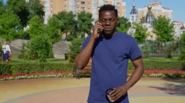 Cep telefonuyla konuşan Afro-Amerikalı bir adam kahve için kağıt bardak tutuyor.