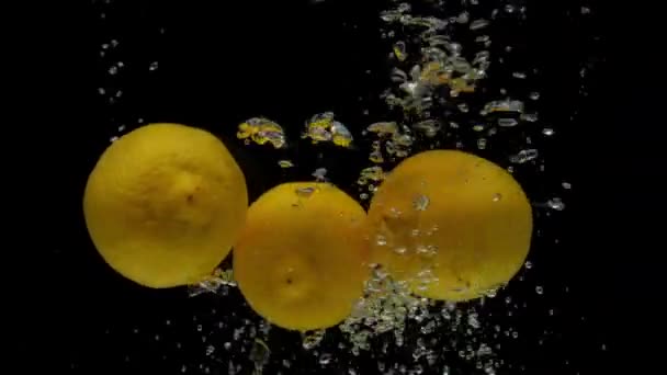 Limone giallo rallentato che cade in acqua trasparente su fondo nero — Video Stock