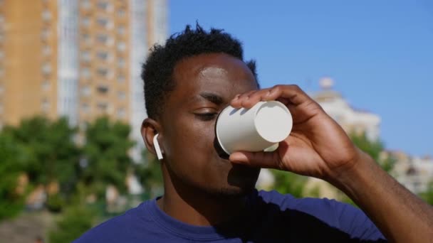 近视笑着的身穿无线耳机的非洲裔美国人喝咖啡茶 — 图库视频影像
