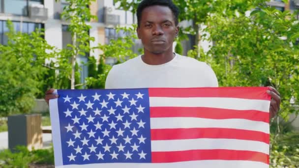 Zbliżenie kamery afro-amerykański mężczyzna trzyma amerykańską flagę i wygląda jak kamera — Wideo stockowe