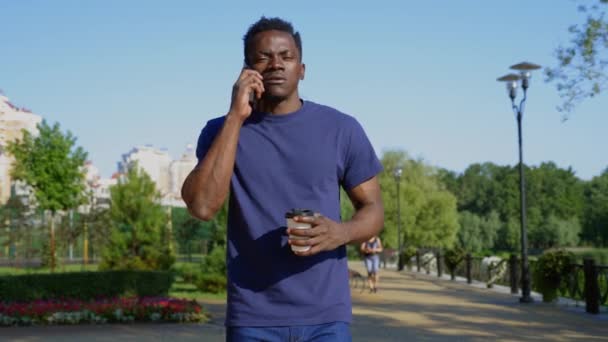 Hombre afroamericano utiliza teléfono móvil sosteniendo taza blanca con café o té en la mano — Vídeos de Stock