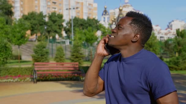 アフリカ系アメリカ人の男が公園に立って携帯電話で話していると周りを見回す — ストック動画