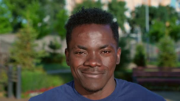 Zamknij się uśmiechnięty afro-amerykański człowiek patrzy aparat fotograficzny na tle parku w lecie — Wideo stockowe