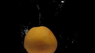 Yavaş çekimde bir greyfurt siyah zeminde şeffaf suya düşüyor.