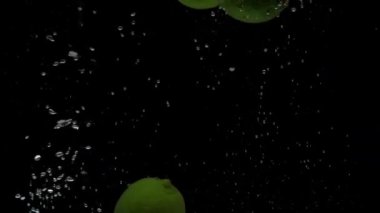 Yavaş çekim üç kireç siyah zemin üzerinde şeffaf suya düşüyor