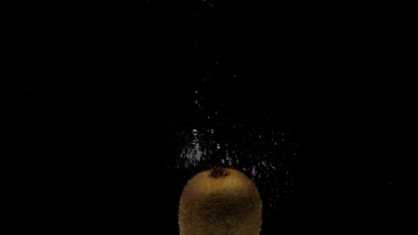 Cámara lenta un kiwi girando cayendo en agua transparente sobre fondo negro — Vídeos de Stock