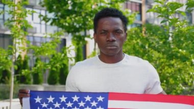Amerikan bayrağını tutan Afro-Amerikan adam kameraya bakıyor.