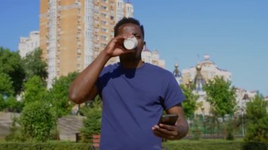 Kablosuz kulaklıklı Afro-Amerikalı işadamı akıllı telefon kullanıyor ve kahve içiyor.