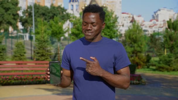 Homem afro-americano sorridente aponta tela do smartphone com tela verde — Vídeo de Stock