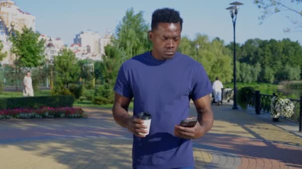 L'uomo afro-americano utilizza il telefono cellulare che tiene in mano la tazza bianca con caffè o tè — Video Stock