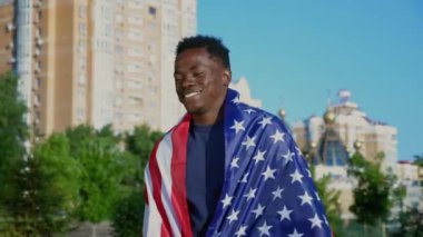 Gülümseyen Afro-Amerikan adam yazın Amerikan bayrağıyla sokakta yürüyor.