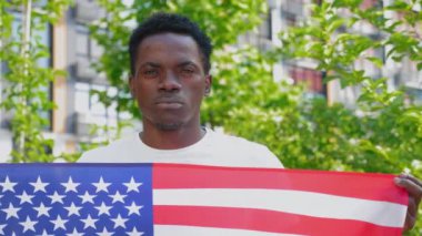 Amerikan bayrağını tutan Afro-Amerikan adam kameraya bakıyor.