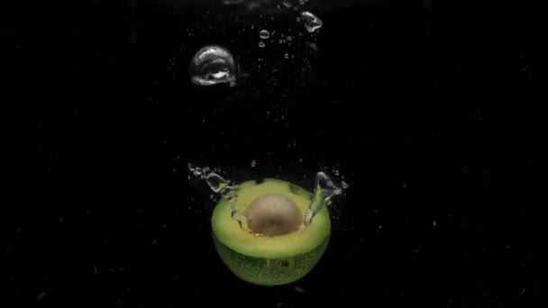 Slow motion avocado helften vallen in transparant water op zwarte achtergrond — Stockvideo