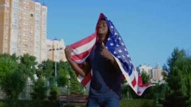 Mutlu Afrikalı adam omuzlarında ABD bayrağı ile parkta yürüyor. Bağımsızlık Günü