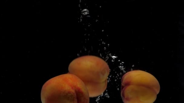 動きが遅い黒の背景に透明な水に落ちる3つの桃 — ストック動画