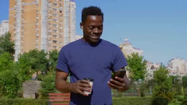 Porträtt Afrikansk man bär trådlösa hörlurar använder smartphone dricka kaffe — Stockvideo