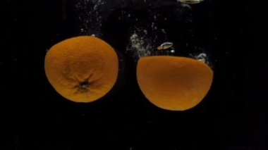 Yavaş çekim portakal yarıları siyah arkaplanda şeffaf suya düşüyor