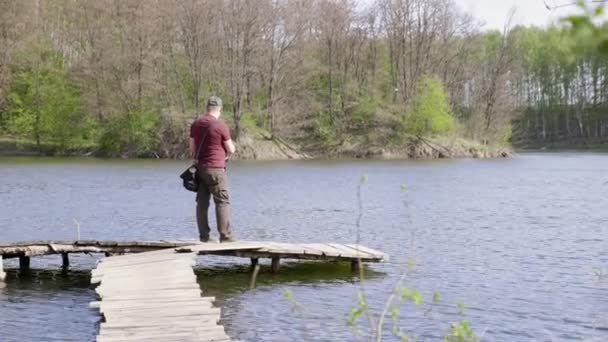 Pescador de tiro ancho captura peces mientras está de pie en un puente de madera — Vídeo de stock