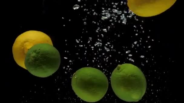 Slow motion citron och lime faller i transparent vatten på svart bakgrund — Stockvideo