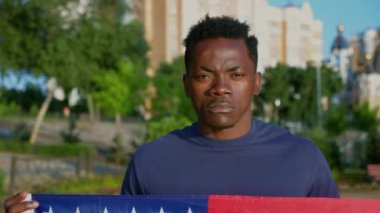 Vatansever Afro-Amerikalı adam Amerikan bayrağı tutuyor ve kameraya bakıyor.