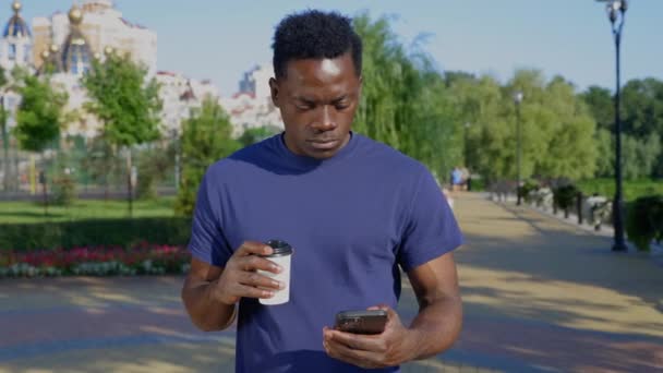 Porträtt afro-amerikansk man frilansare använder smartphone innehav kopp med kaffe — Stockvideo