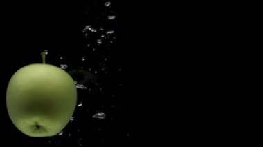 Slow motion one green apple spinning falling into transparent water on black background. Beautiful fresh fruit splashing in aquarium. Organic fruits, healthy food, diet, air bubbles