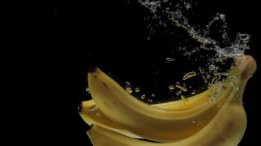 Yavaş hareket eden muzlar siyah arkaplanda şeffaf suya düşüyorlar. Akvaryuma taze meyve sıçraması. Sağlıklı yemek, diyet, hava kabarcıkları